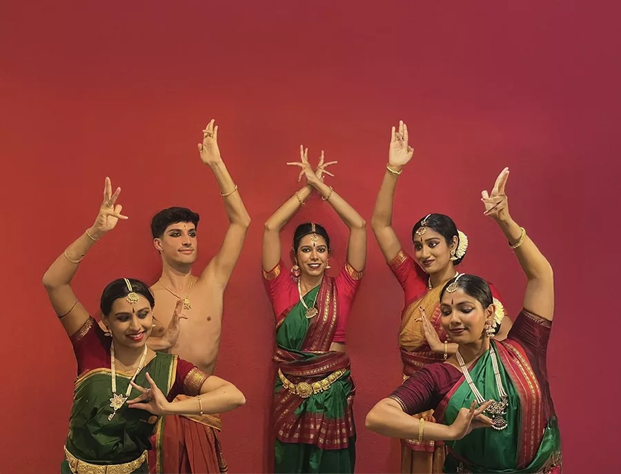Group of dancers for the Ganesh Chaturthi Barcelona 2025. Four girls and Francisco Valiente posing with a bharatanatyam pose in a red background with colorful saris.